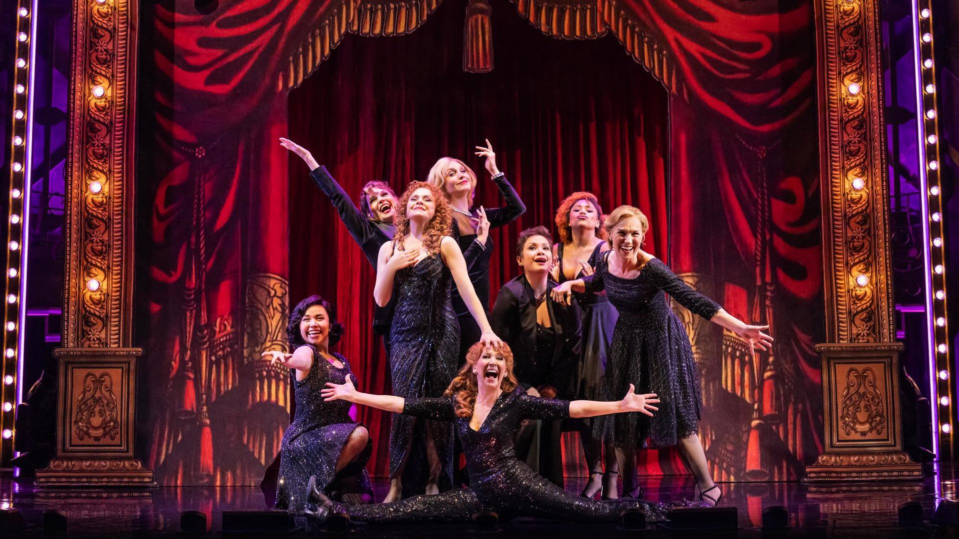 Eight performers pose exaggeratedly in a formation.