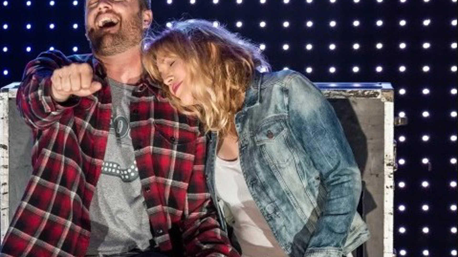 couple sitting, the woman is laying head on his shoulder while he sings