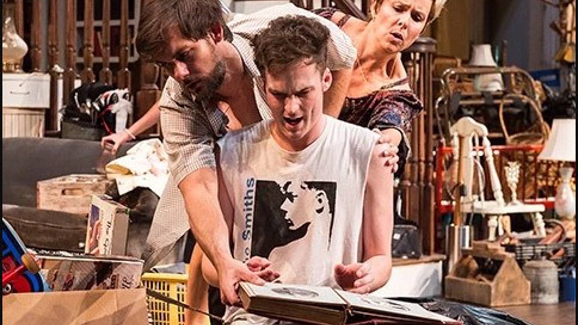 3 characters in the play Appropriate looking over each other's shoulders at a photo album