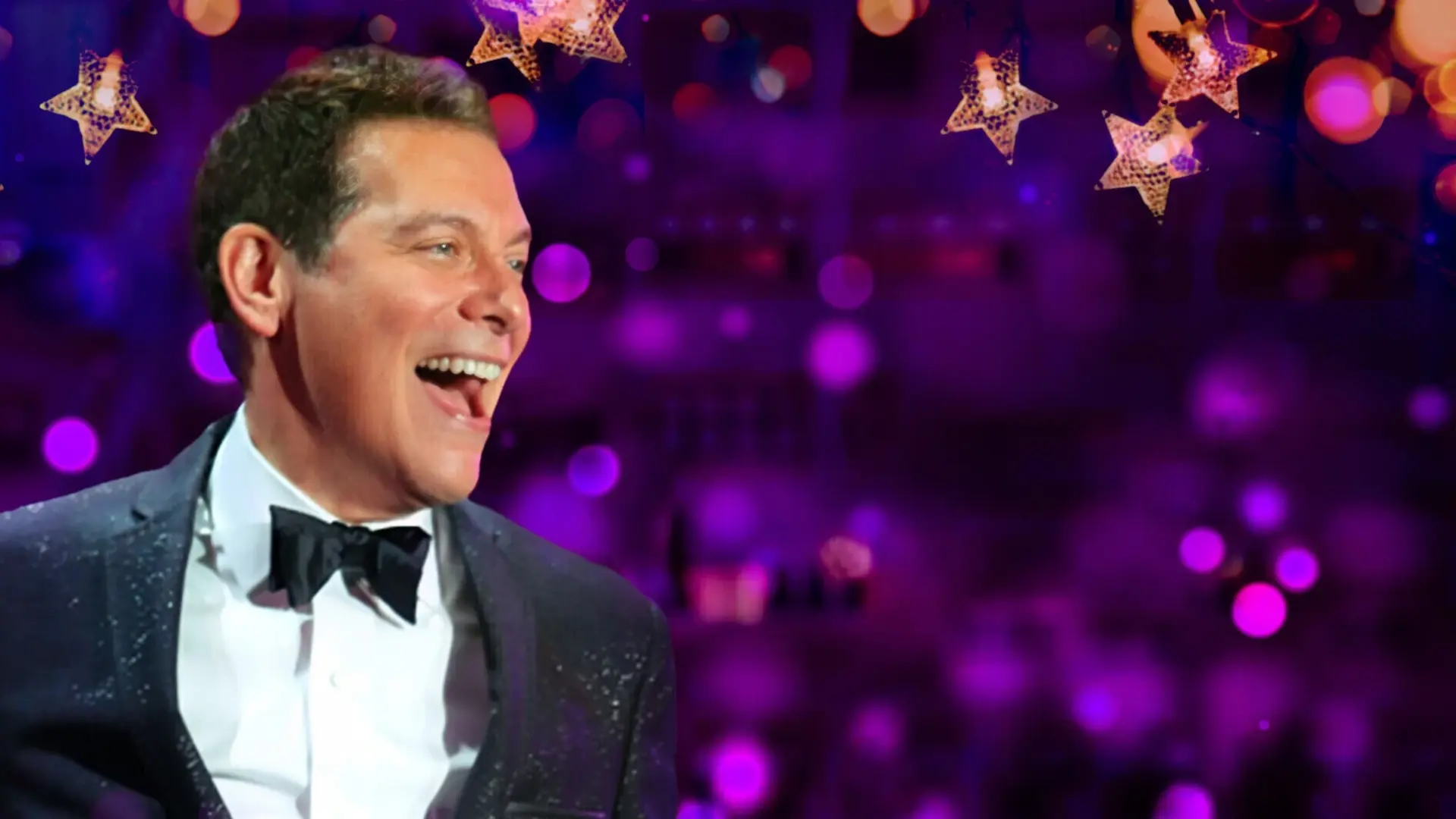 Michael Feinstein in a tuxedo, in front of a sparkling purple background. 