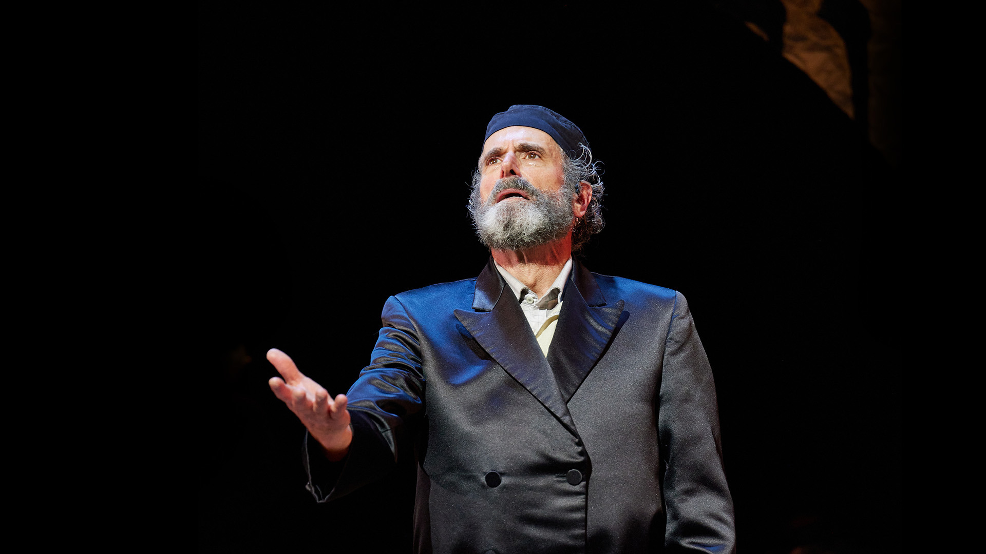 An actor wearing all black reaches out with one hand. 