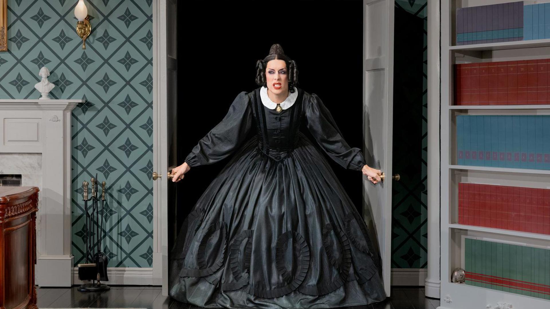 An actress in a black dress bursts through a set of double doors with a scowl on her face.
