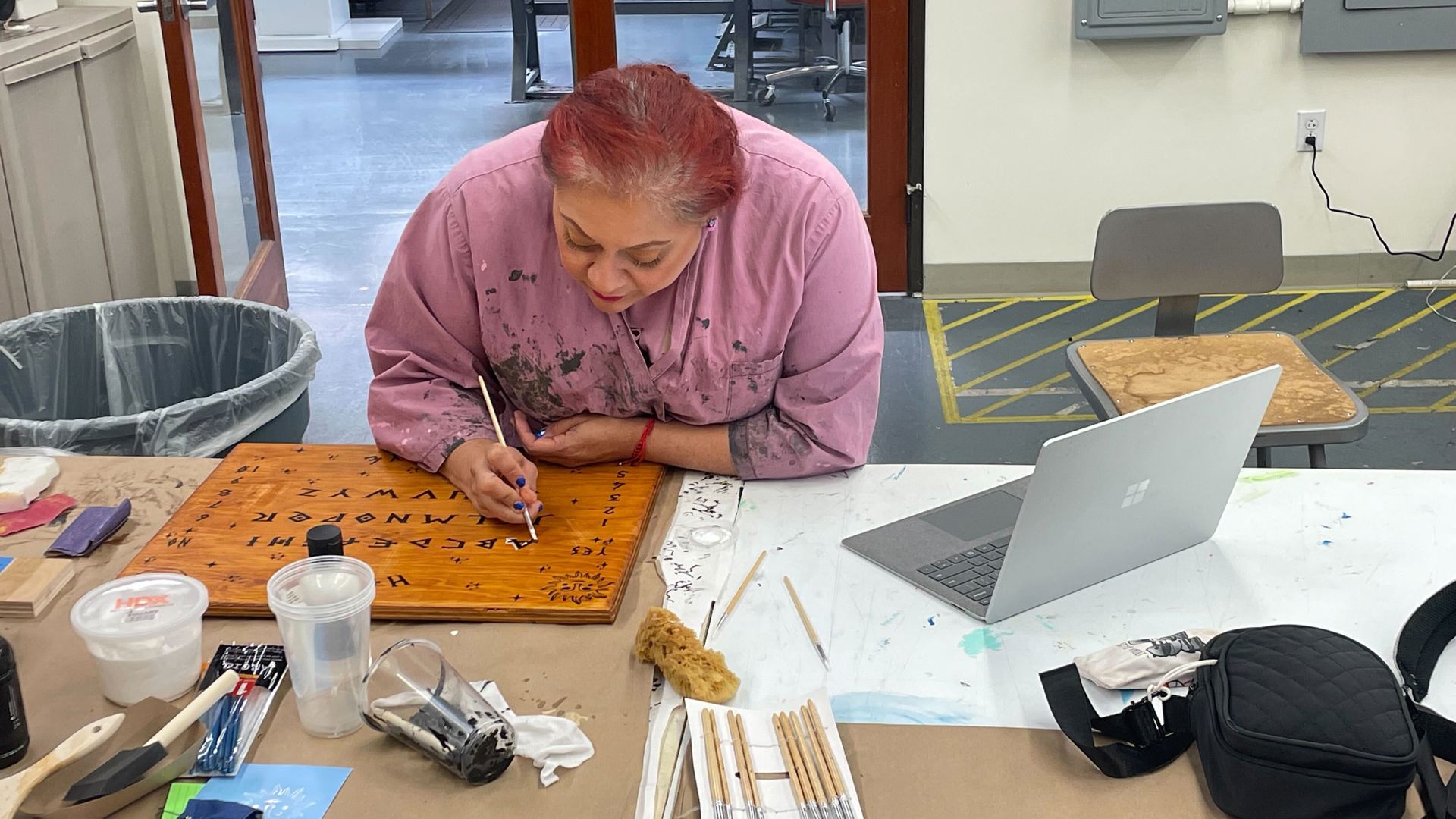 An apprentice paints lettering on a prop ouiji board.