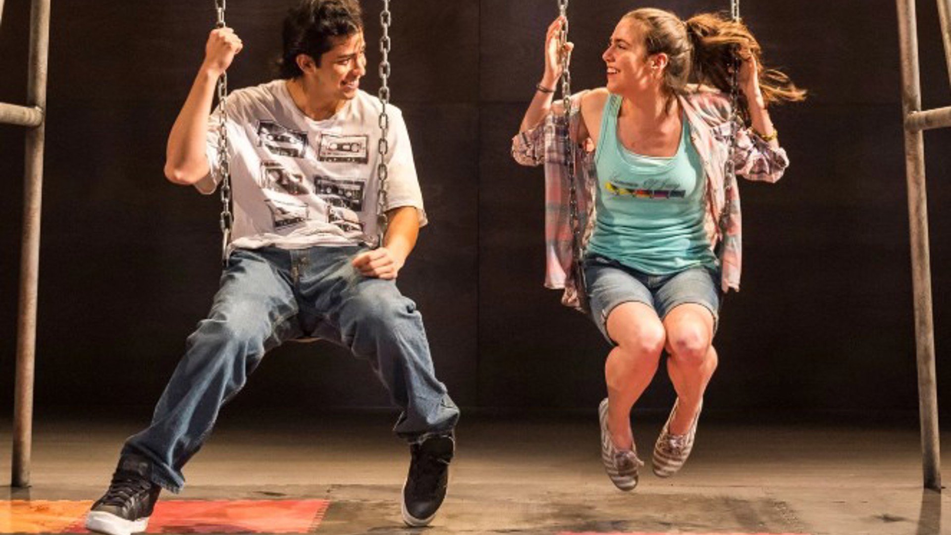 actress and actor sitting on swings smiling on stage at the Kirk Douglas Theatre
