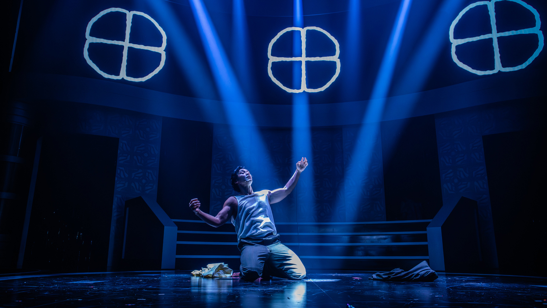 A performer kneels down on their knees with their arms held open.