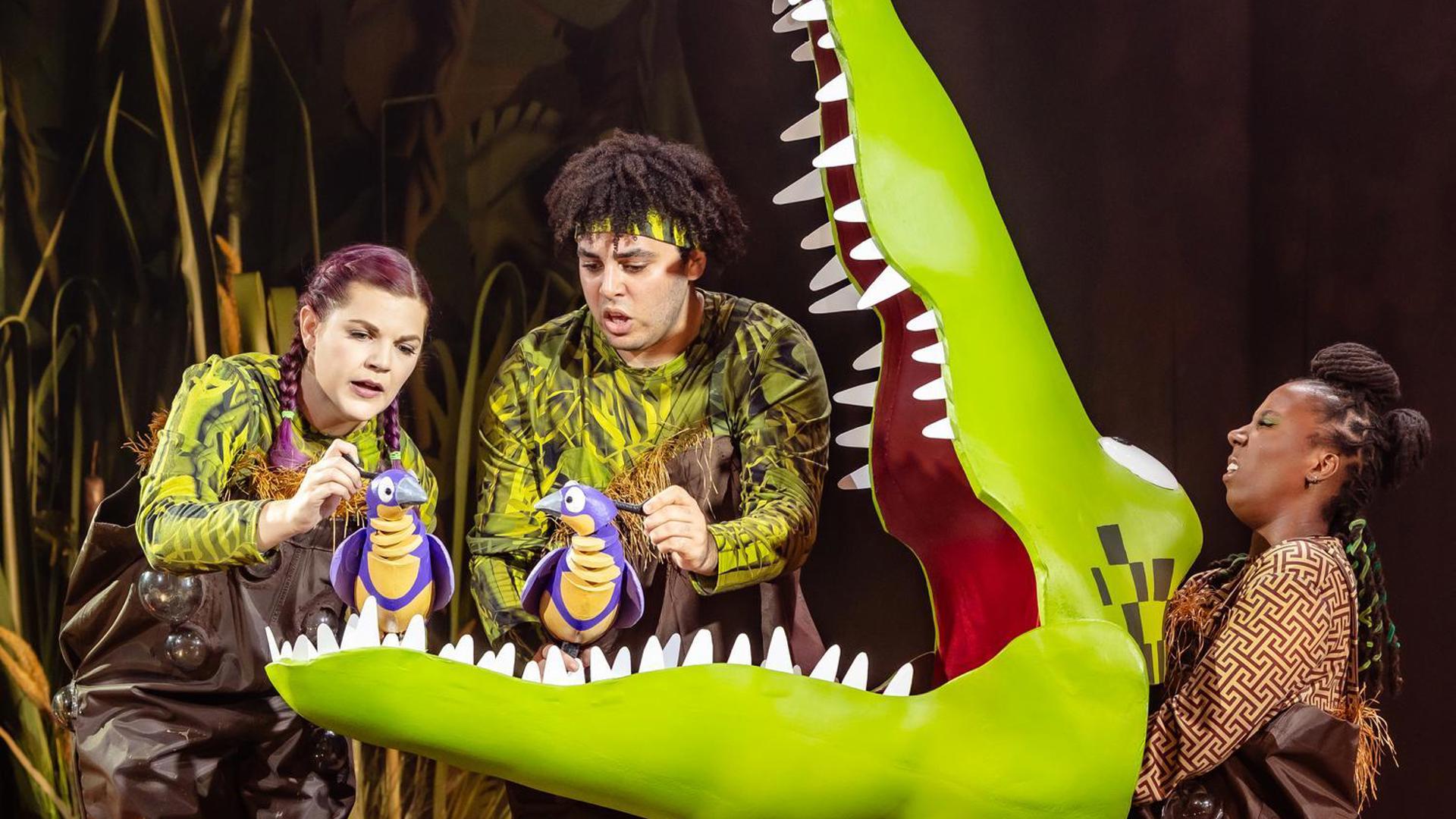 Two small birds sitting in the wide open jaws of The Enormous Crocodile.