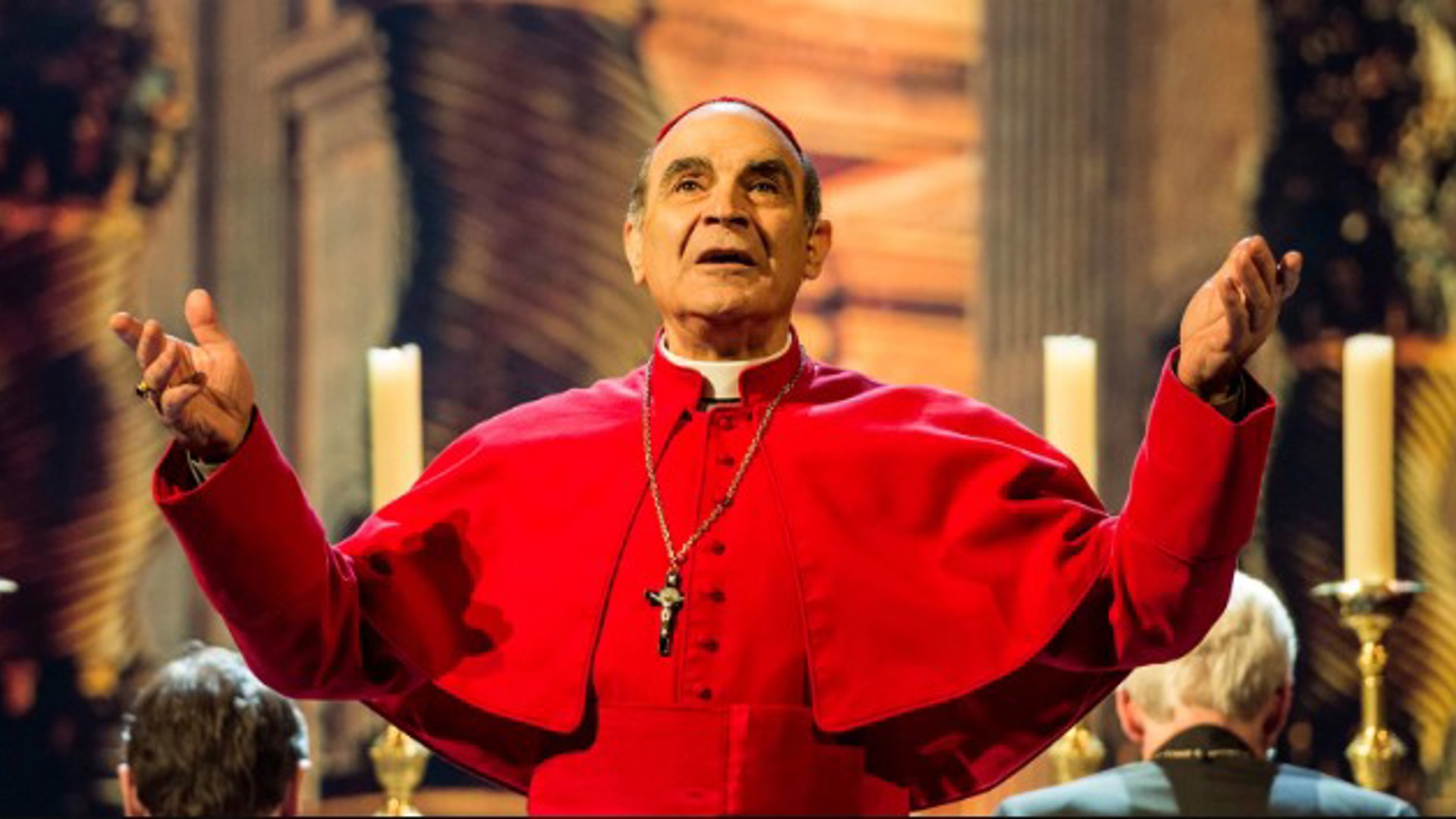 David Suchet in a Cardinals costume with hands up praising in the play The Last Confession