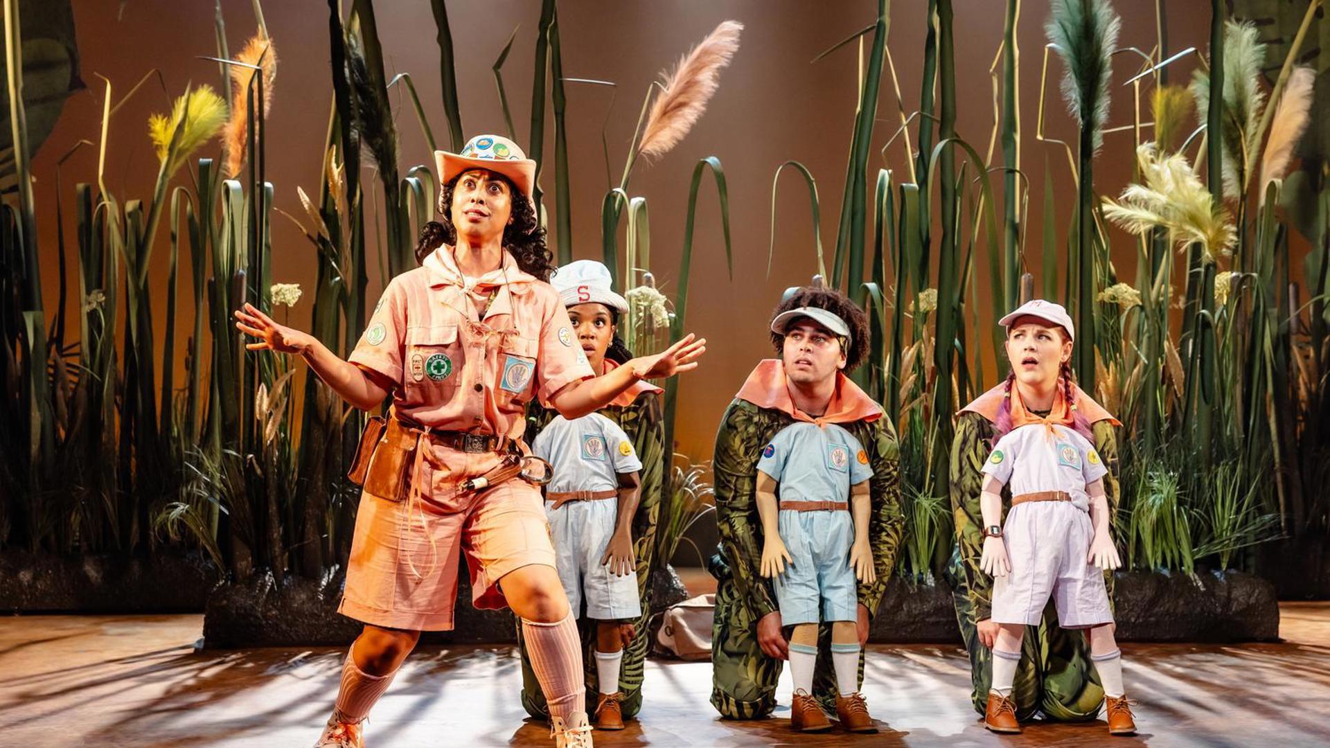 A scout leader presenting in front of three young scouts, portrayed by adults on their knees.