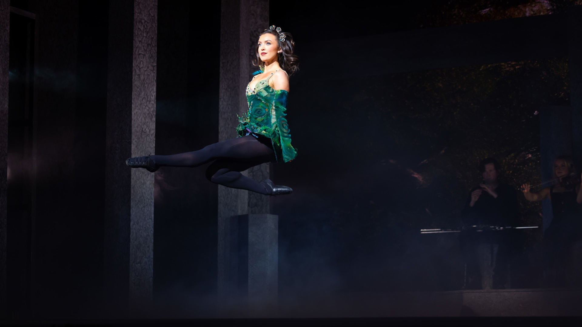 A performer jumping in the air on stage with one leg extended.