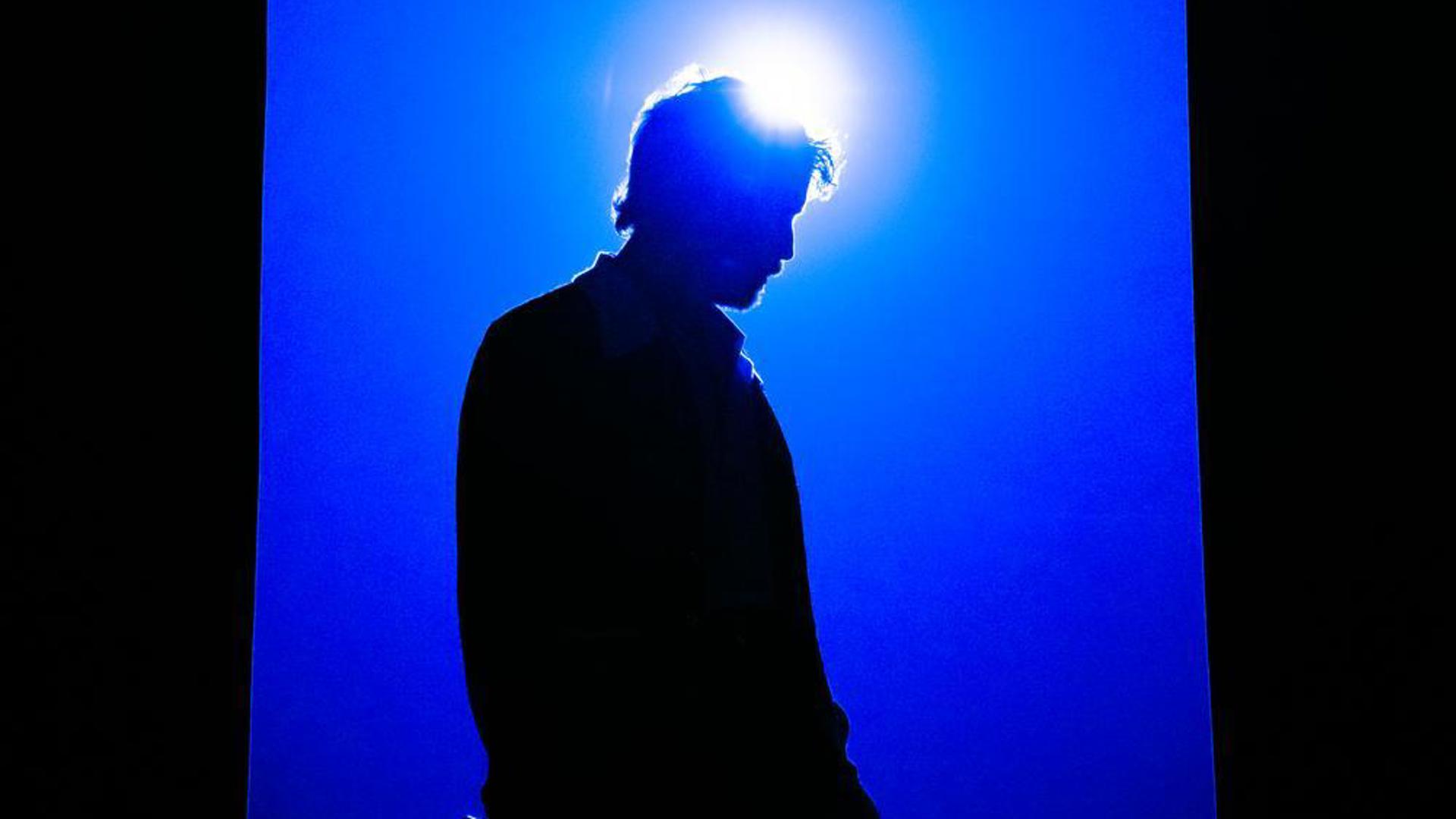 Bright blue spotlights shine a silhouette of Ben Platt.