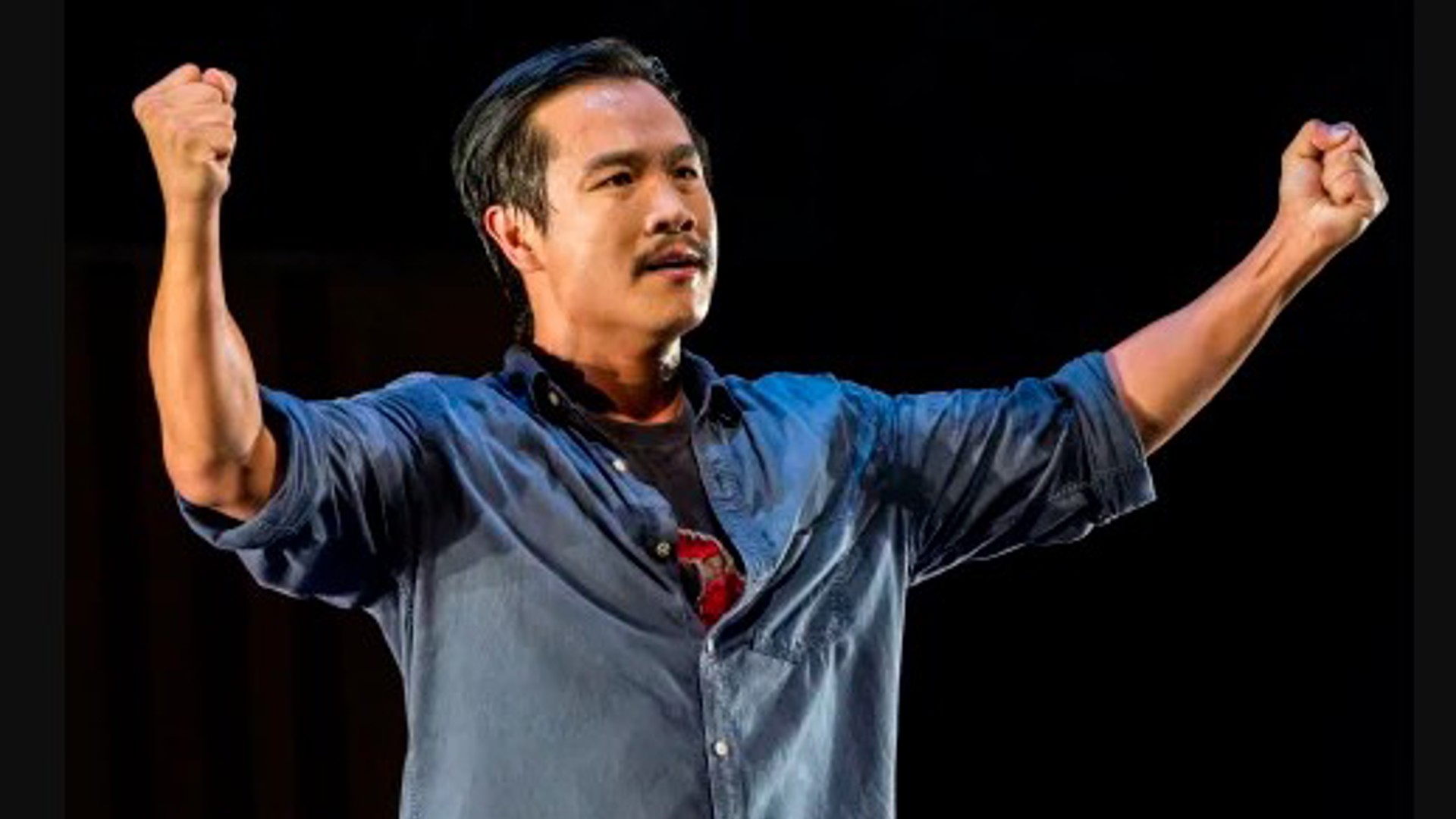 Trieu Tran standing on stage with arms up and open in a one man play