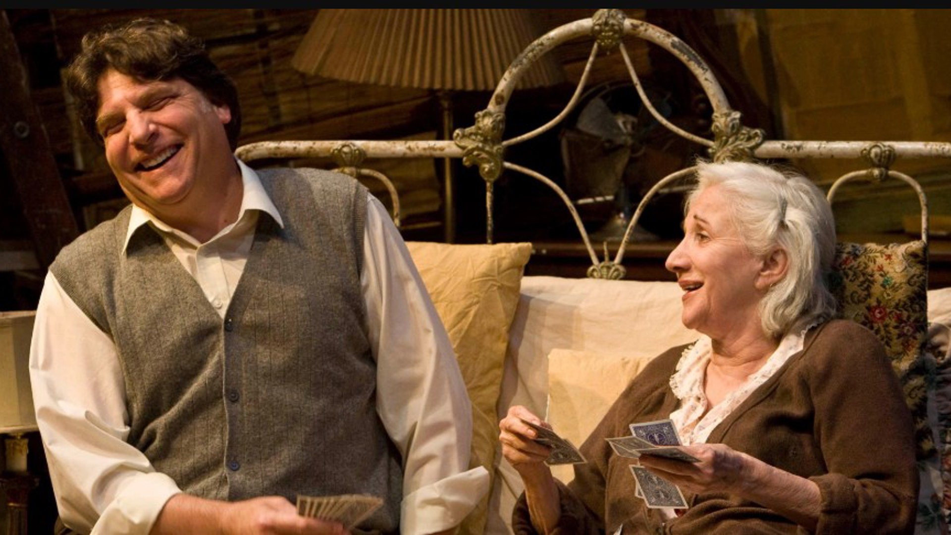 Marco Barricelli and Olympia Dukakis sitting, smiling, acting on stage in the play Vigil