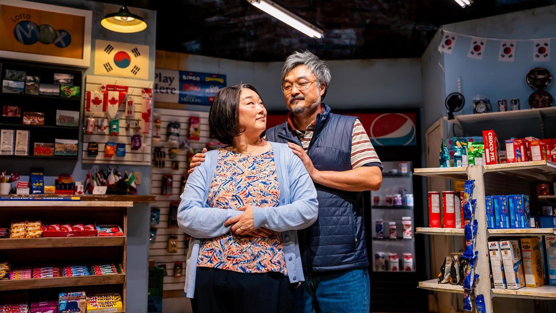 A couple stands together inside a convenience store, looking at each other warmly.