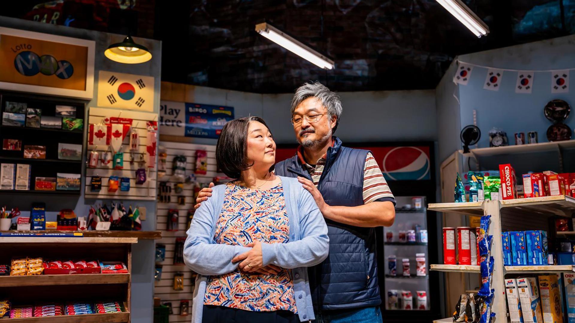 A couple stands together inside a convenience store, looking at each other warmly.