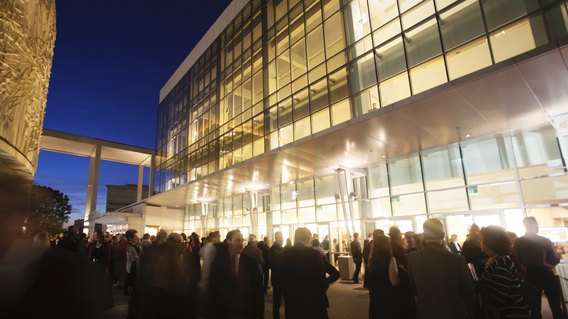 A photo of a brightly lit building at night with many people walking around the outside in a blur