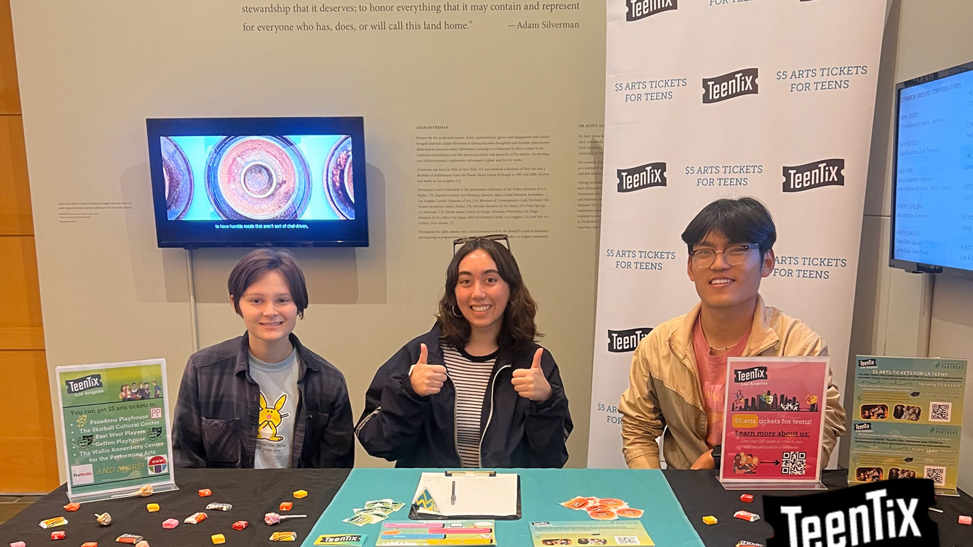 Three teens sit behind a table with TeenTix flyers and candy. 