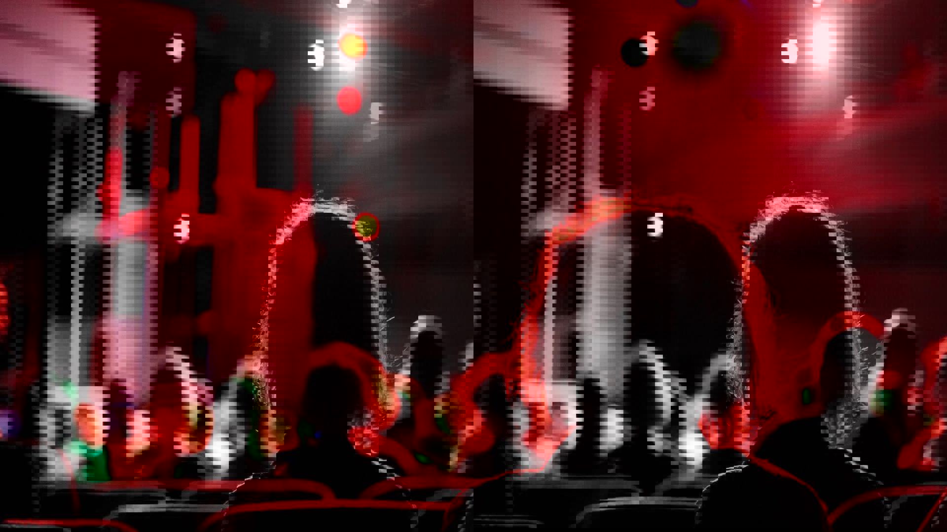 The silhouette of an individual seated in a theatre illuminated by a red light.