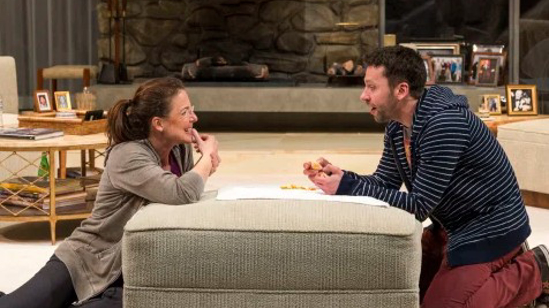 woman and man in a living room on either side of an ottoman happily conversing