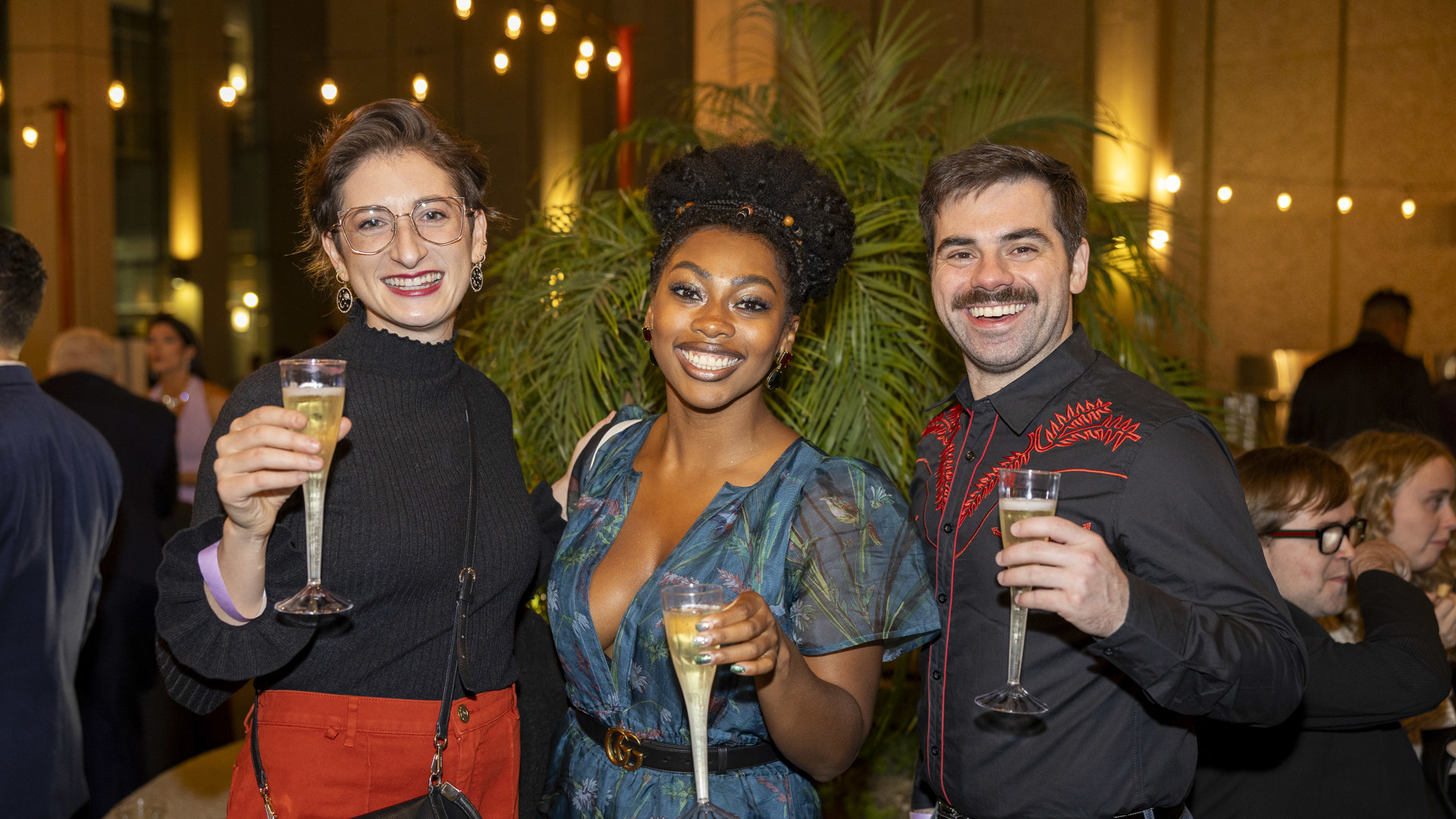 Three people smile and hold up champagne.