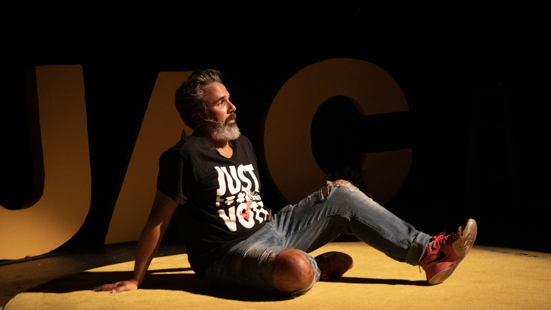Manuel Oliver sits on a stage in front of giant letters spelling GUAC
