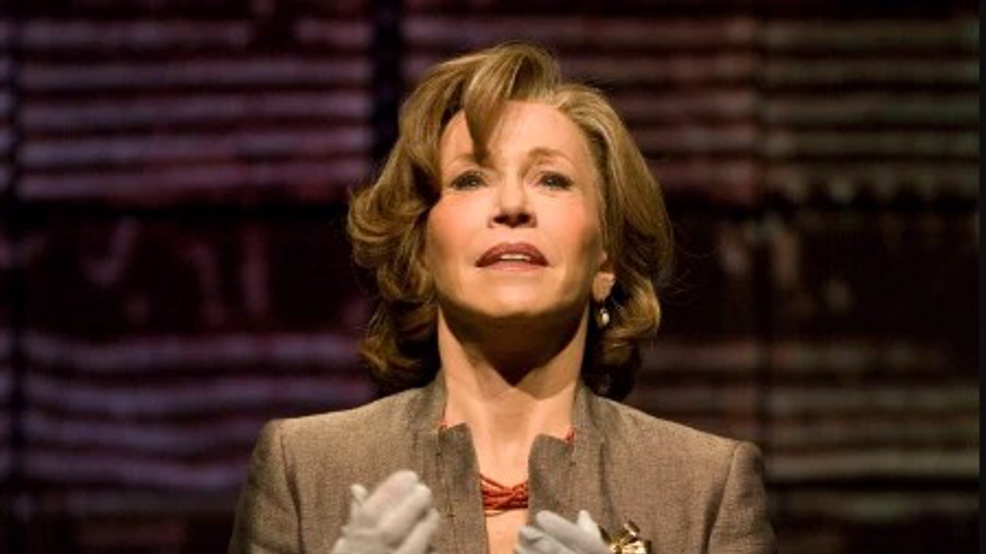 Jane Fonda standing looking forward with hand forward wearing white gloves