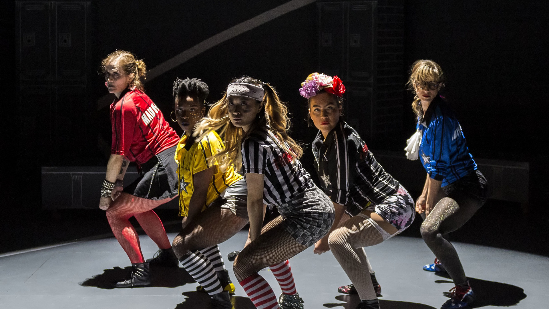 Five actors squat onstage during a performance.