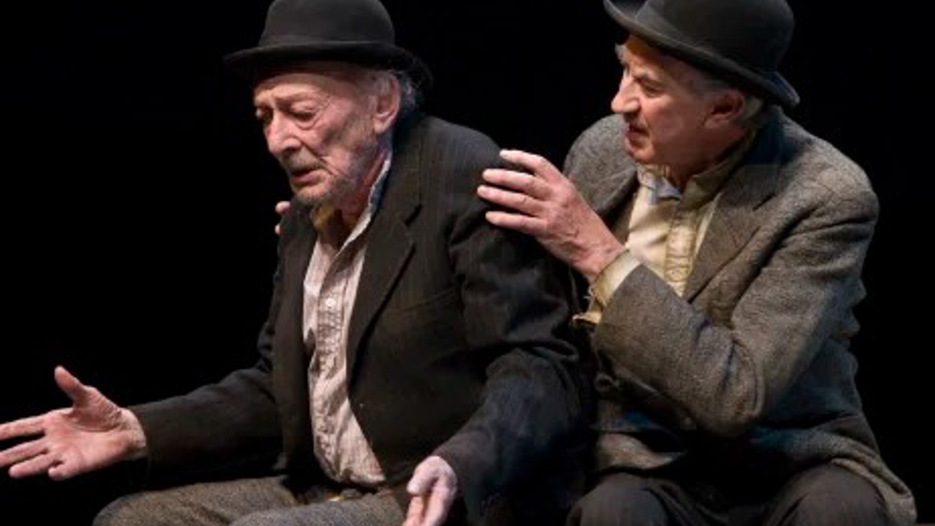 two men in bowler hats and tweed suits, one is consoling the other