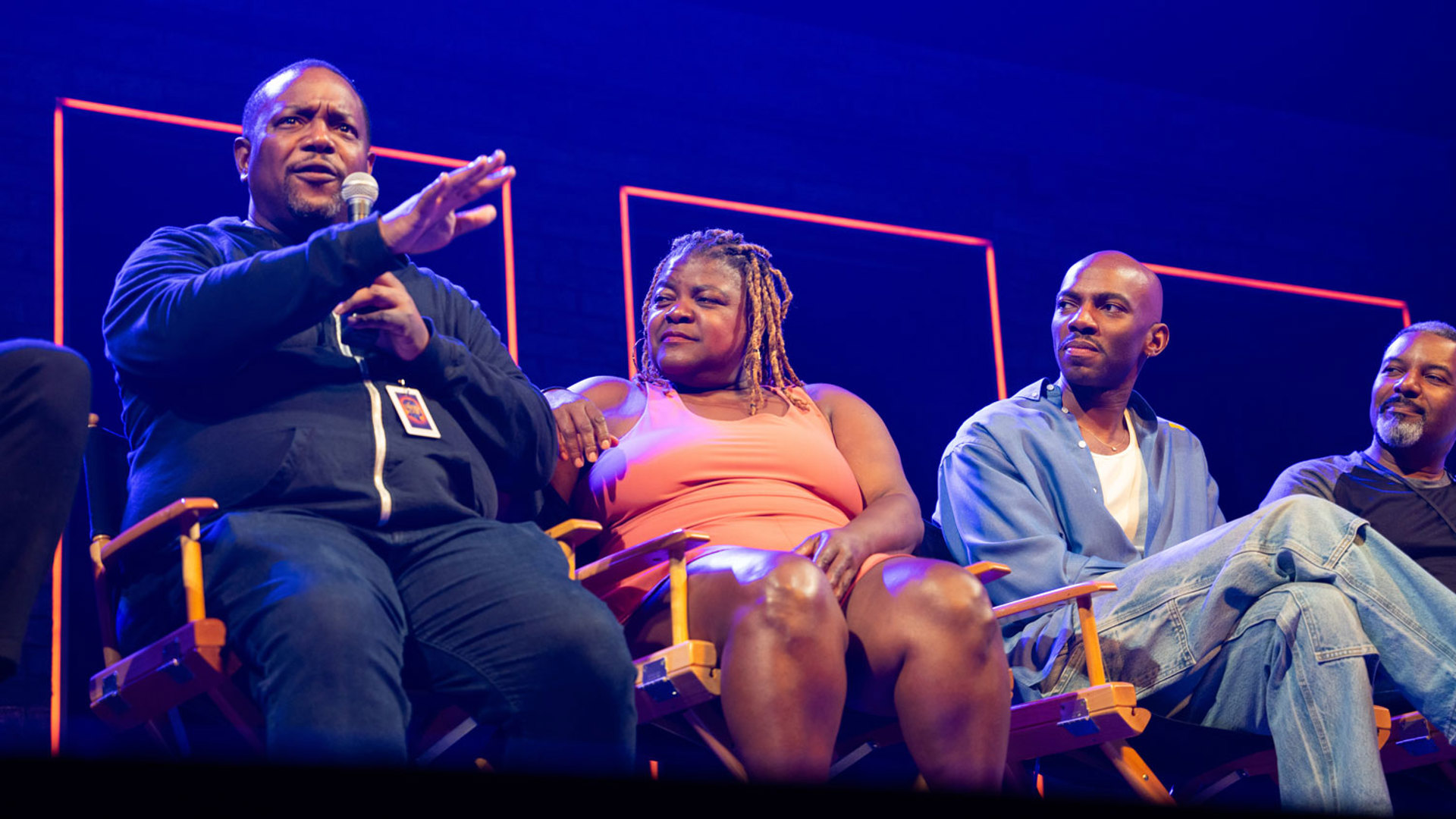 A panel of actors sit on the set of 'A Strange Loop', one of them is speaking into a mic. 