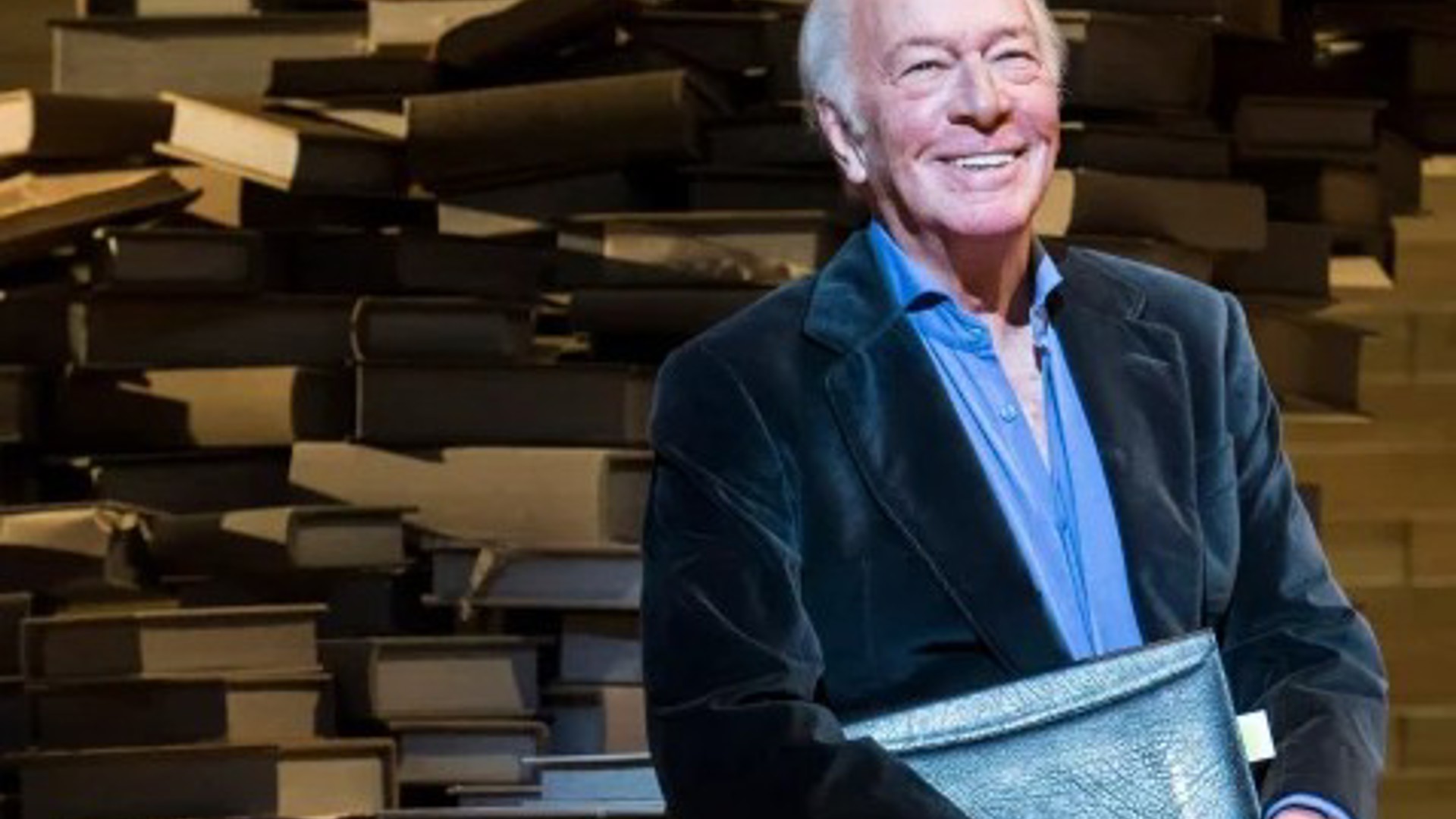 Christopher Plummer on stage in front of stacks of books in Los Angeles Theatre