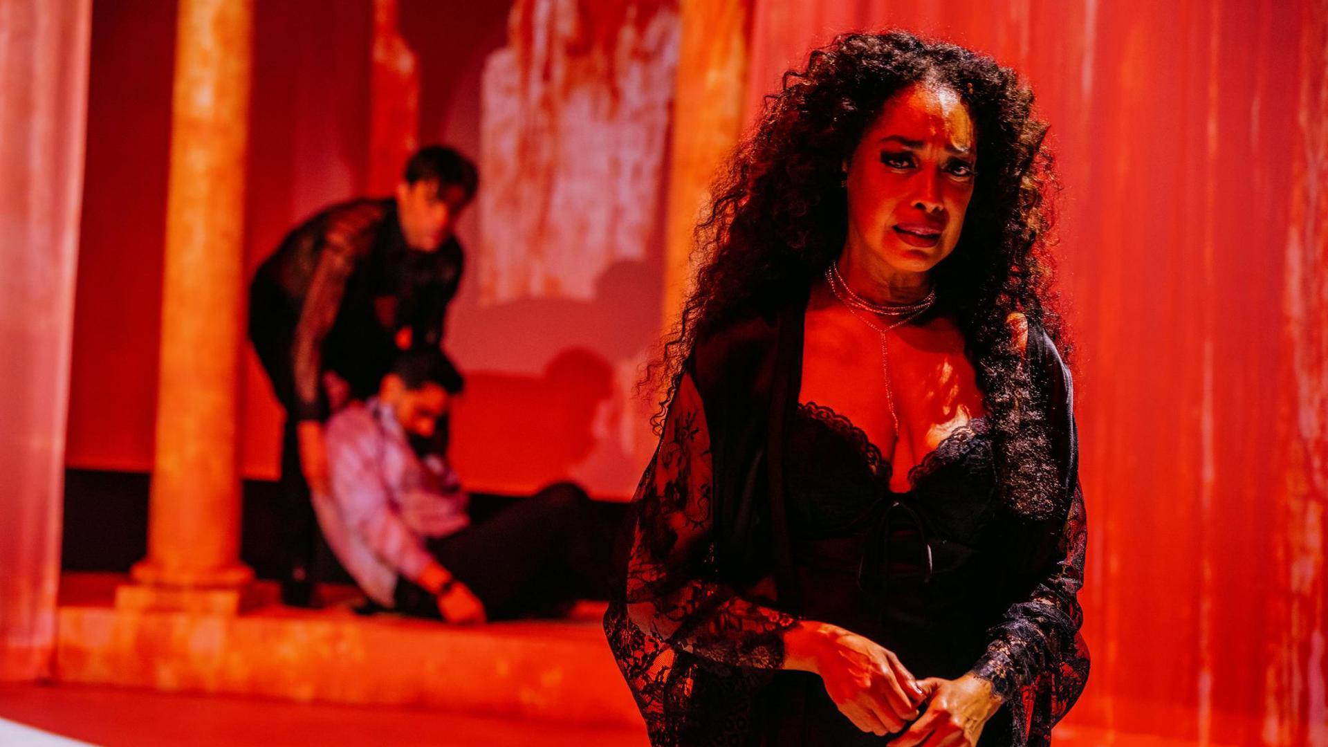An actor looks distressed while, upstage, an actor drags a limp body on the floor.