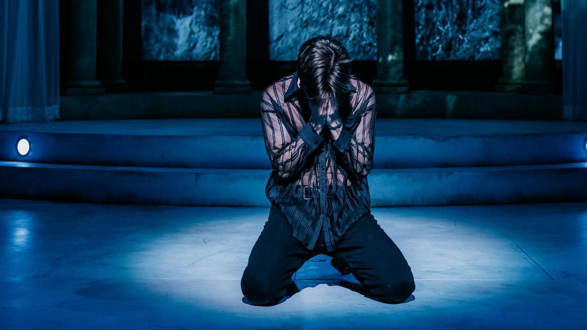 An actor sits on their knees, with their hands covering their face in distress.