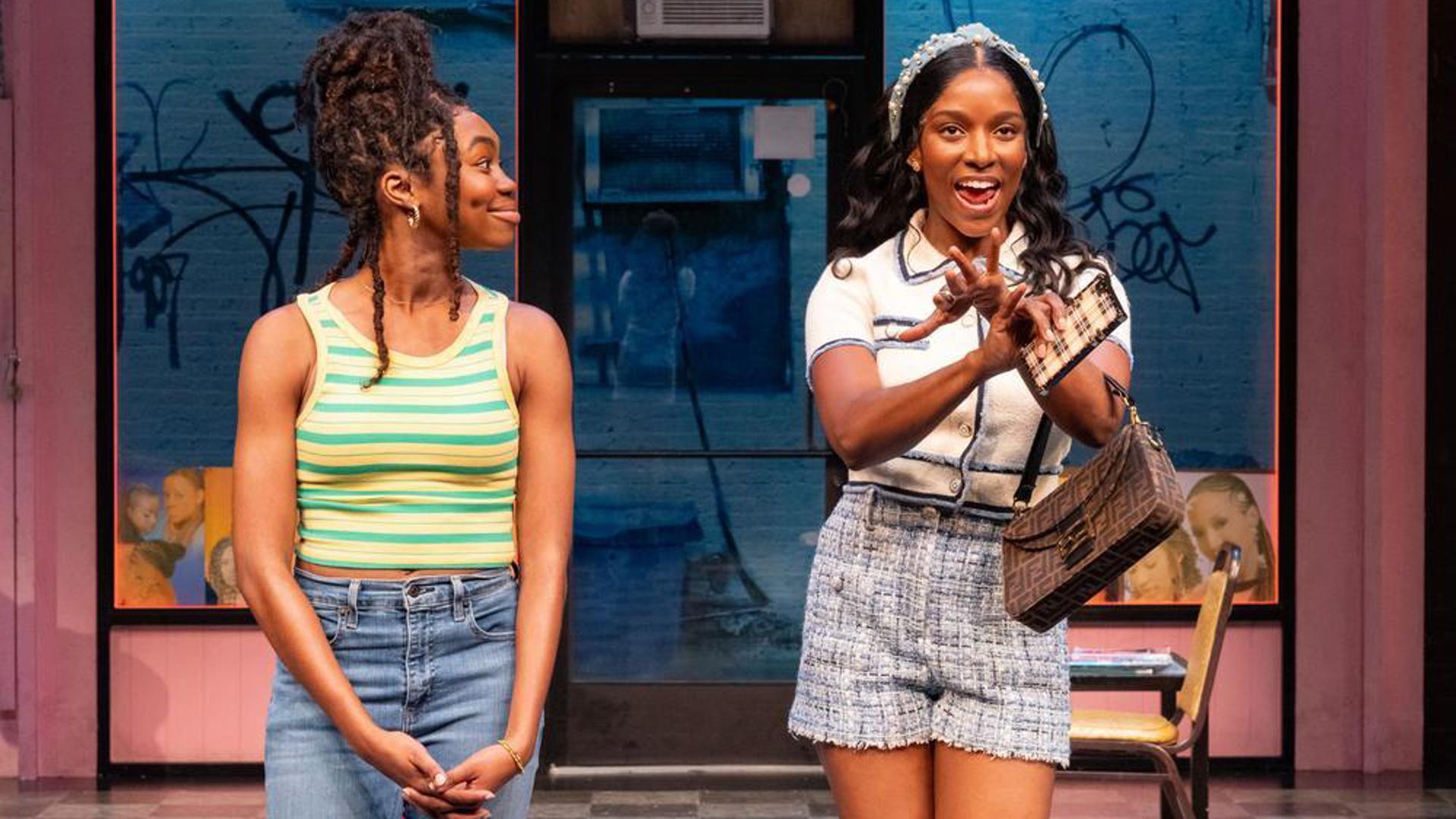 Two performers stand center stage. One speaks animatedly while the other watches them.