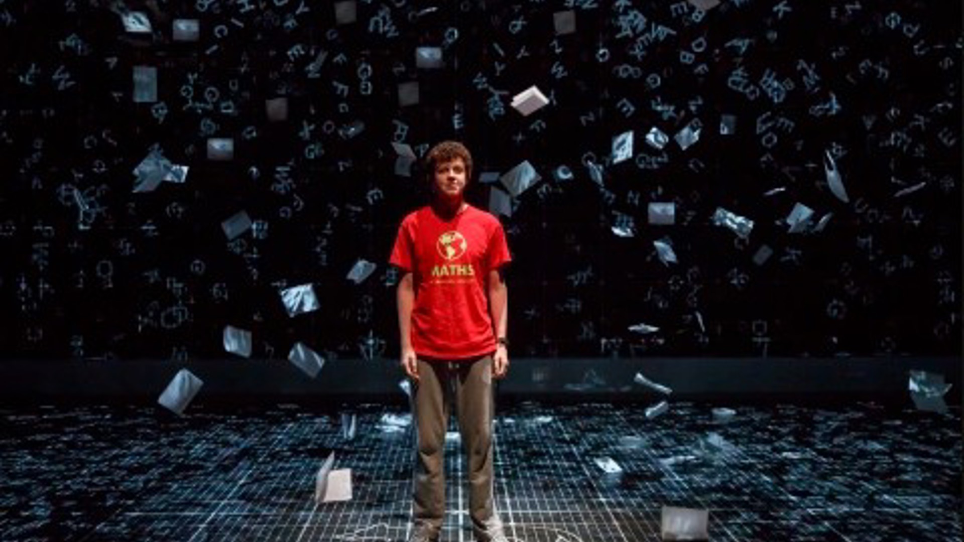 intelligent 15-year-old Christopher standing on stage surrounded by papers falling around him
