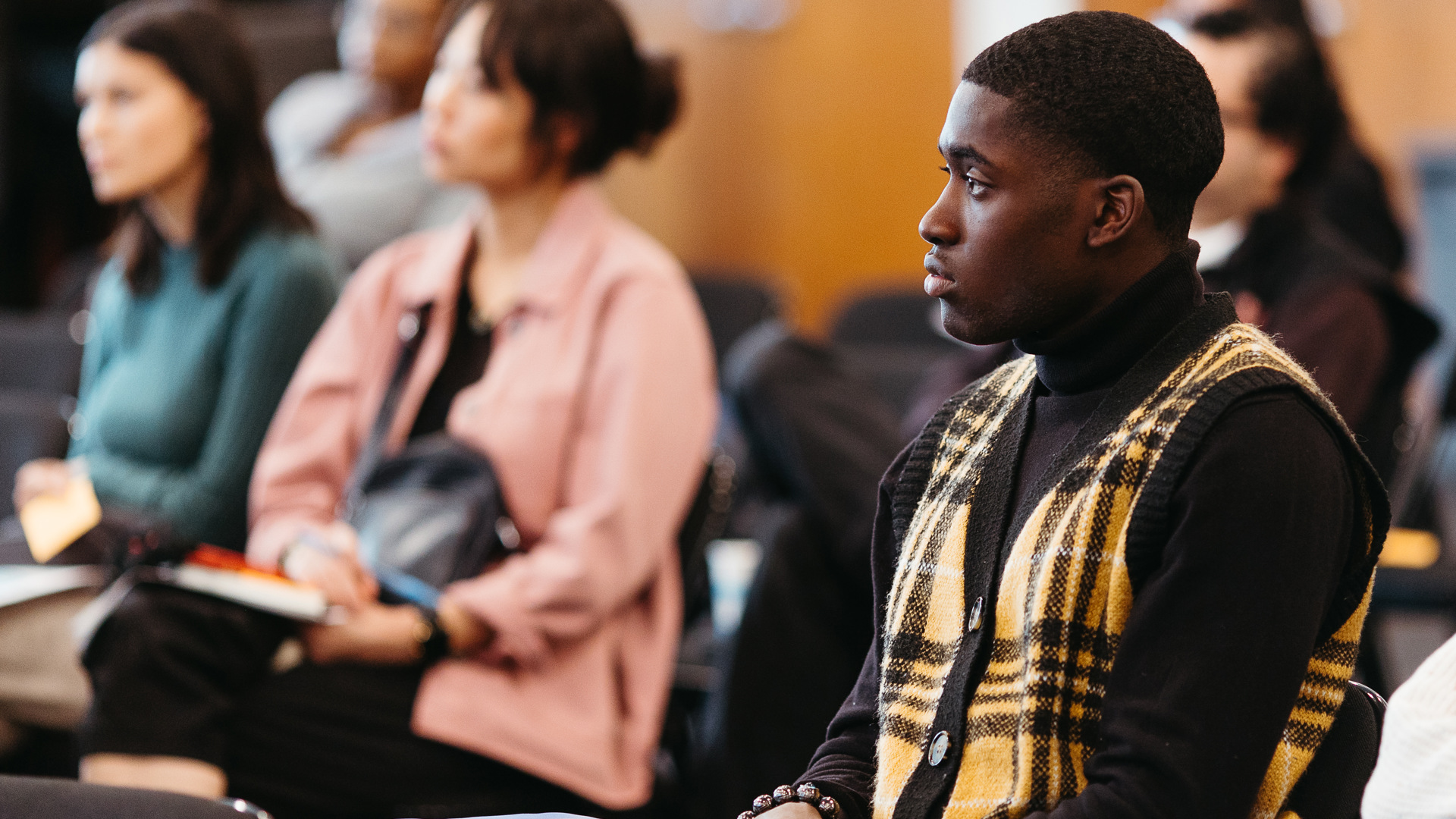 A group of young adults sit and listen. 