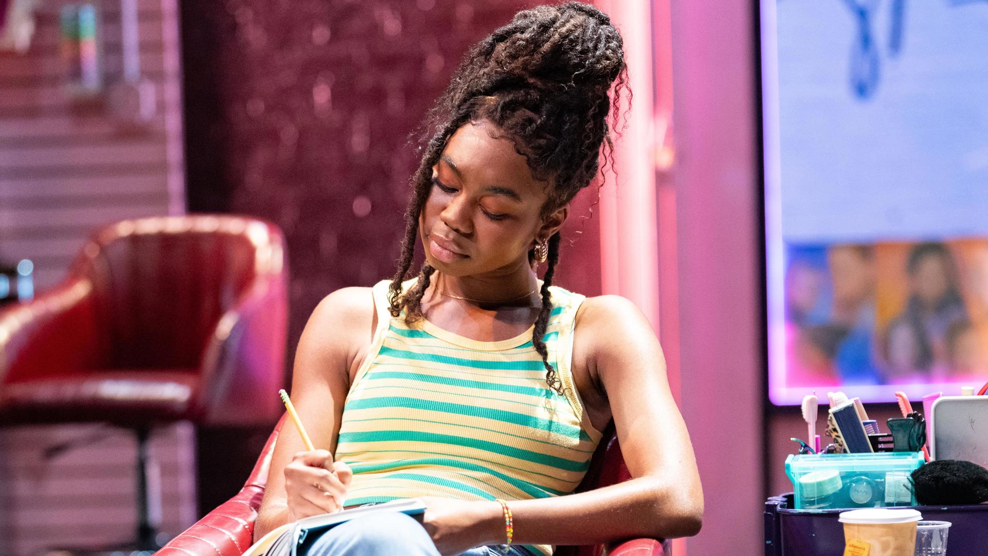 A performer sits in a chair and writes in a journal.