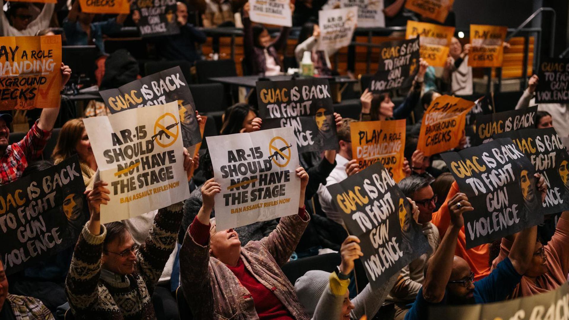 Audience members hold out signs "AR-15 should not have the stage."