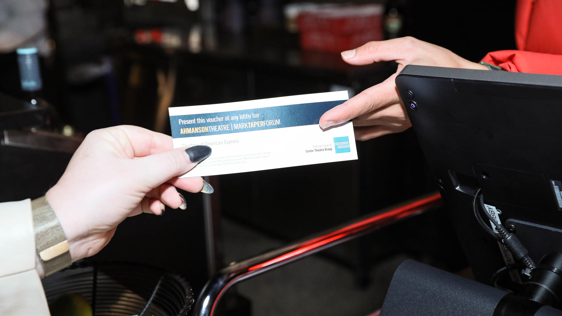 Box office representative hands patron tickets in a ticket envelop. 